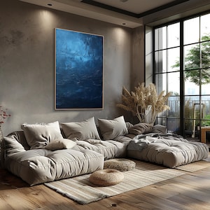 Puede incluir: Una gran pintura abstracta en tonos azules cuelga de una pared en una sala de estar moderna. La pintura est&aacute; sobre un gran sof&aacute; seccional gris claro con una manta y almohadas. La habitaci&oacute;n tiene una ventana grande con vista a los &aacute;rboles y un balc&oacute;n.