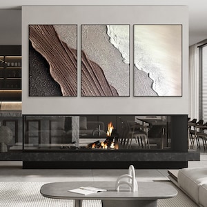 May include: Three abstract paintings in black frames, each depicting a different section of a beach scene with brown, white, and beige colors.