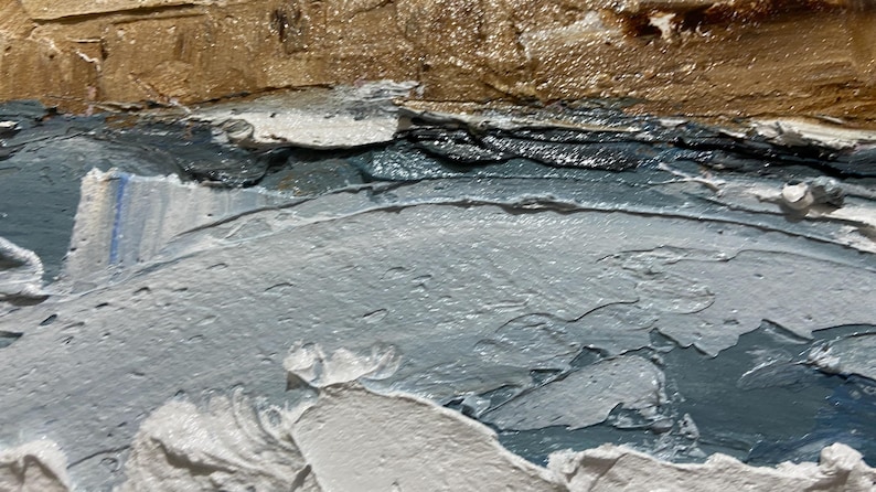 May include: Close-up of an abstract painting with textured brushstrokes. The artwork features layers of color, including shades of gray, blue, and brown, creating a sense of depth and movement. The thick application of paint adds a tactile quality.