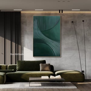 May include: A large, abstract wall art piece with a textured, dark green design. The artwork features curved lines and a gold frame. The piece is displayed above a green sofa in a modern living room setting.