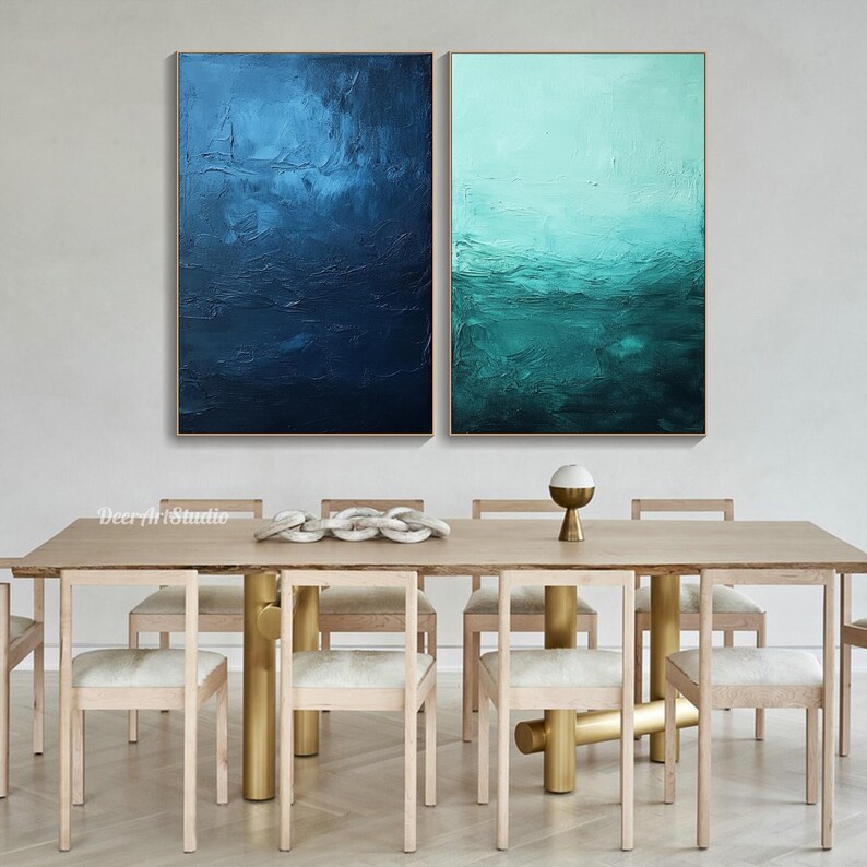Puede incluir: Dos pinturas abstractas en un comedor moderno. Las pinturas son en tonos de azul y verde, con un efecto texturizado de pinceladas. Las pinturas est&aacute;n colgadas en una pared blanca sobre una mesa de madera con patas doradas. La mesa est&aacute; puesta con seis sillas y un cuenco de objetos decorativos.