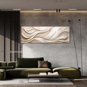 May include: Abstract wall art featuring a beige and white textured design with flowing lines. The art is displayed on a wall in a living room setting with a green sofa and a coffee table.