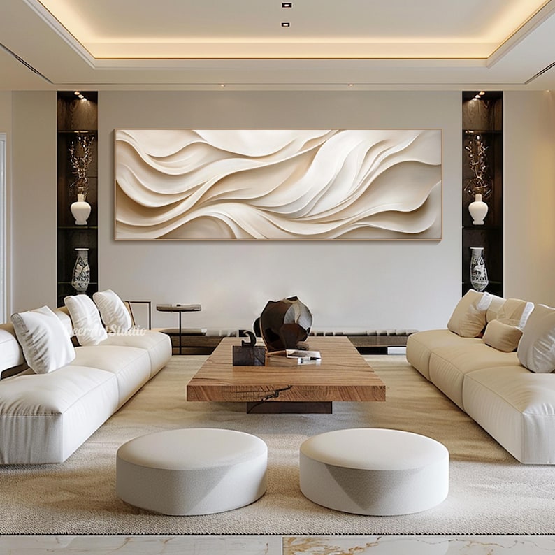 May include: A modern living room with a white and beige abstract wall art piece above a white sectional sofa. The room features a wooden coffee table with a decorative object on top, and two white ottomans.