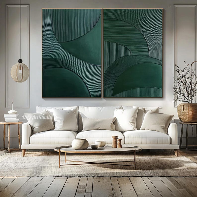 May include: Two-panel abstract wall art featuring a textured, dark green design. The artwork has a series of curved lines and shapes, creating a sense of depth and movement. The art is framed in a light-colored wood and hangs above a white sofa.