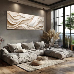 May include: A large, abstract painting with white and beige waves hangs above a sectional sofa with plush cushions. The sofa is in a modern living room with large windows and a view of trees.