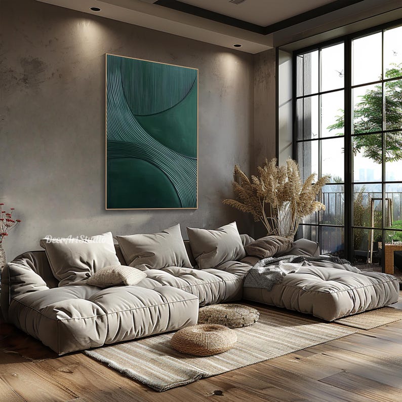 May include: A modern living room featuring a large, modular beige sofa with multiple cushions. A green abstract painting hangs on the gray wall. The room has a large window with a view of greenery and a wooden floor.