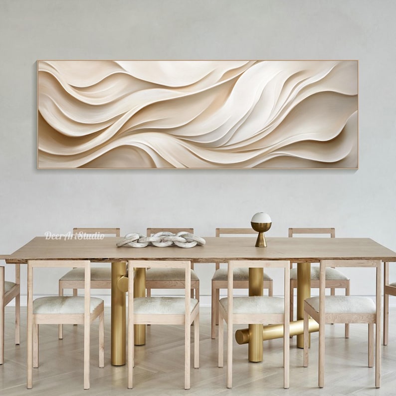 May include: A large abstract painting with flowing, white and beige lines hangs above a wooden dining table with six chairs. The table has a natural wood finish and gold metal legs. The chairs are also made of wood and have white cushions.