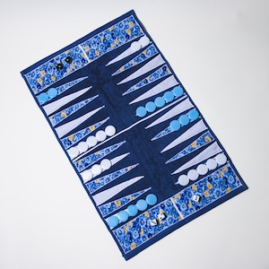 May include: A navy blue backgammon board with white and blue game pieces. The board has a floral patterned border in blue, yellow, and white. Two dice are visible, along with black and white checkers.