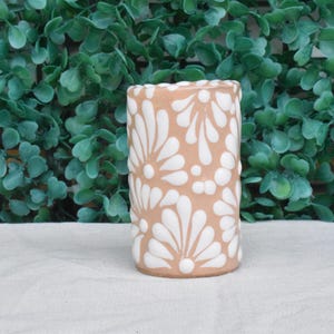 Puede incluir: Un jarr&oacute;n de cer&aacute;mica de color terracota con un patr&oacute;n floral blanco. El jarr&oacute;n tiene una forma cil&iacute;ndrica y est&aacute; decorado con un patr&oacute;n repetitivo de flores estilizadas.