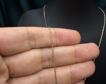 May include: A gold chain necklace with a delicate, textured design. The chain is thin and has a subtle shimmer.