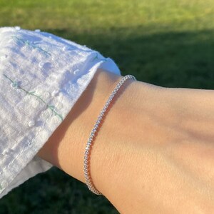 May include: A silver tennis bracelet with small, clear stones.