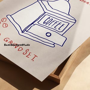 May include: A hand-drawn illustration of a coffee grinder with the word "COFFEE" written on it. The illustration is in blue ink on a white background. The text "GROUND SET" is written in red ink below the illustration.
