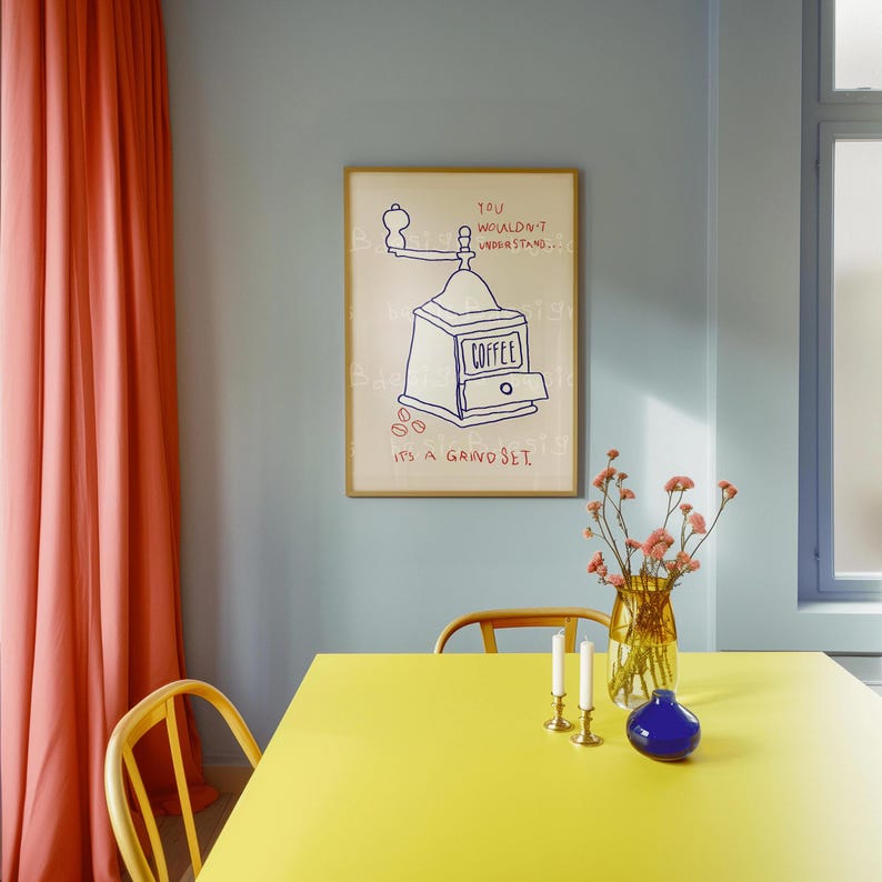 May include: A yellow table with a blue vase of pink flowers, two candlesticks, and a blue vase. A framed print with a hand-drawn illustration of a coffee grinder and the text "You wouldn't understand... It's a grindset." hangs on the wall behind the table.