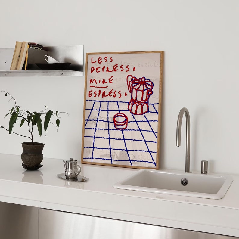 May include: A framed print with a white background and blue grid pattern. The print features red and blue text that reads "Less Depresso More Espresso." A red and white illustration of a coffee pot is on the print.