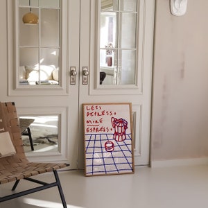 May include: A framed print with a white background and blue grid pattern. The print features red text that reads "Less Depresso More Espresso" and a red and white illustration of a coffee pot.