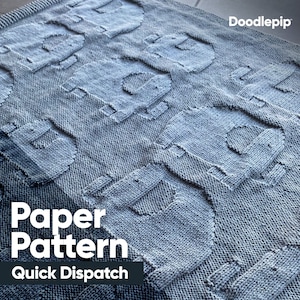 May include: A grey knitted baby blanket with a repeating pattern of stylised robots. The blanket has the text "Paper Pattern" and "Quick Dispatch" printed on it.