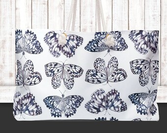 Puede incluir: Bolsa de lona blanca con estampado de mariposas en blanco y negro. La bolsa tiene dos asas de cuerda blanca.
