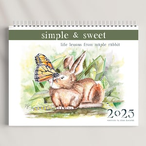 May include: A watercolor illustration of a brown rabbit with a butterfly on its nose. The rabbit is surrounded by green leaves and the text "simple & sweet life lessons from maple rabbit 2025 watercolor by alina skoczek" is at the bottom of the image.