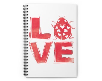May include: A white spiral-bound notebook with the word "LOVE" in red, stylized block letters. A red ladybug with heart-shaped spots is next to the word. The notebook is on a white background.