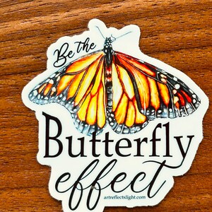 May include: White sticker with a black and orange butterfly and the text "Be the Butterfly effect" and the website "artreflectslight.com" at the bottom.