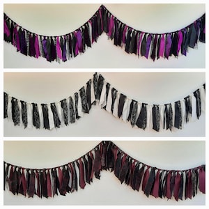 May include: Three fabric rag garlands hanging in a draped formation. The top garland features black and purple strips. The middle garland consists of black, white, and spiderweb-patterned strips. The bottom garland displays black and dark red strips.