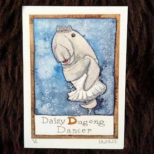 Könnte beinhalten: Aquarellillustration einer Dugong-Tänzerin namens Daisy, die eine Krone und einen Tutu trägt. Das Kunstwerk ist vor einem blauen Hintergrund mit Blasen platziert, in einem braunen Rahmen eingefasst und enthält das Datum 29.09.22.