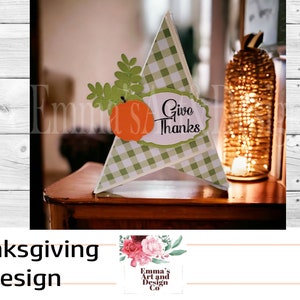 May include: A green and white checkered paper cone with a cut-out pumpkin and leaves. The cone has a white oval with the text "Give Thanks" on it. The cone is sitting on a wooden table.