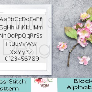 May include: A framed cross-stitch pattern featuring a block alphabet in black thread on white fabric. The letters and numbers are displayed in a grid. Pink and white flowers and green leaves are arranged on the right side of the frame. The text "Cross-Stitch Pattern" and "Block Alphabet" are at the bottom.