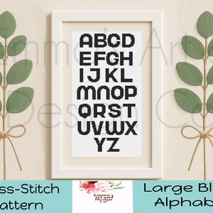 May include: A framed cross-stitch pattern featuring a large block alphabet in black on a white background. The frame is white, and the background is a neutral beige. Green leaf sprigs with twine bows flank the frame. The text "Cross-Stitch Pattern" and "Large Block Alphabet" are at the bottom.