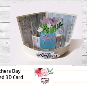 May include: A 3D pop-up card with a curved design. The card features a blue mason jar with a pink bow, filled with pink and white flowers. The card is decorated with a woodgrain pattern and the text "Happy Mother's Day".