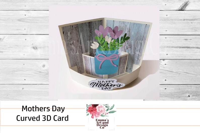May include: A 3D pop-up card with a curved design. The card features a blue mason jar with a pink bow, filled with pink and white flowers. The card is decorated with a woodgrain pattern and the text "Happy Mother's Day".