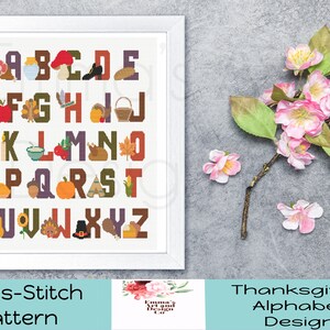May include: A cross-stitch pattern featuring a Thanksgiving alphabet with autumn-themed illustrations. The letters are in a brown, orange, and yellow colour scheme. The pattern includes images of pumpkins, turkeys, acorns, and more.