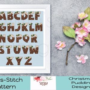 May include: Cross-stitch pattern featuring the alphabet in the shape of Christmas pudding. Each letter is brown with white icing and green holly. The pattern is on a light blue background.