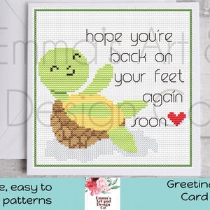 May include: A cross-stitch greeting card with a green turtle and the text "hope you're back on your feet again soon." The card has a green border and a red heart. The card is on a white background.