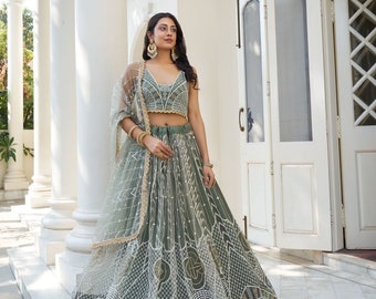 May include: A woman wearing a sage green embroidered lehenga with a matching crop top and a sheer dupatta. The lehenga has a geometric pattern and is adorned with sequins and pearls.