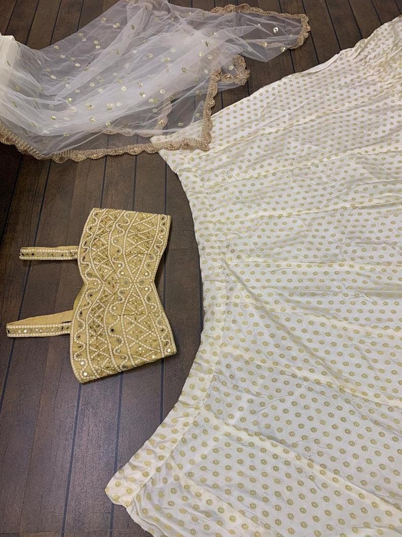 May include: A white skirt with gold polka dots, a matching white and gold embroidered crop top, and a white sheer scarf with gold sequins.