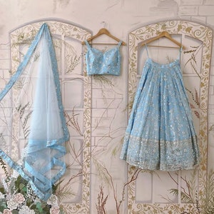 May include: A light blue embroidered lehenga with a matching crop top and a sheer dupatta. The outfit is decorated with silver sequins and beads.