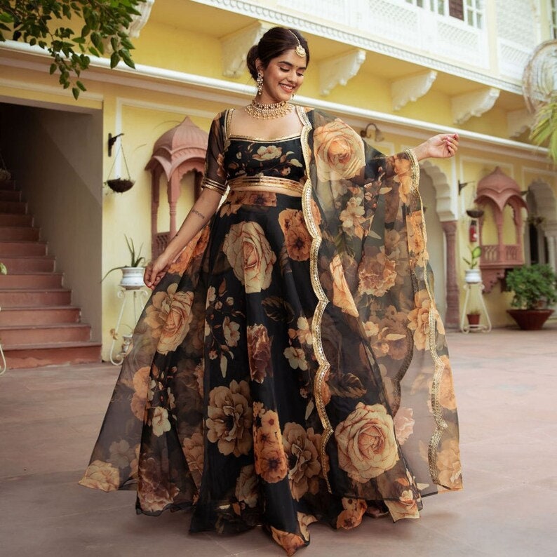 May include: A black and brown floral print maxi dress with a gold belt and a sheer overlay. The dress has a scoop neckline and three-quarter sleeves.