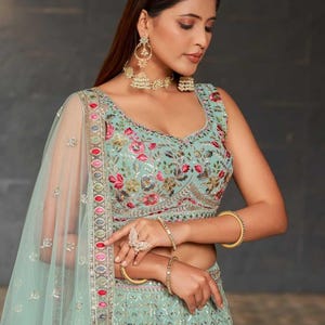 May include: A light turquoise embroidered formal dress with floral patterns and a matching sheer veil. The dress features gold bangles, a ring, and earrings. The text "Blacknboz" is visible on the dress.