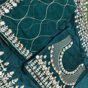 Puede incluir: Un conjunto verde oscuro con intrincados bordados dorados. El conjunto incluye una parte superior con un escote detallado y patrones florales, y una bufanda a juego con un dise&ntilde;o de cuadr&iacute;cula. Los bordes est&aacute;n adornados con ribetes florales dorados.