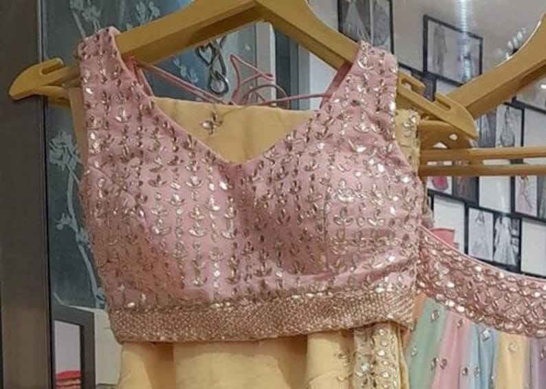 May include: A pink sleeveless blouse with a V-neckline and intricate gold embroidery. The blouse features a delicate floral pattern and a beaded trim.