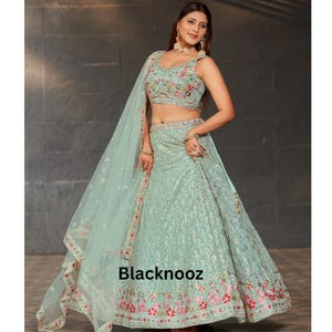 May include: A light green embroidered lehenga with a matching dupatta. The lehenga features floral embroidery in pink, red, and green. The top is sleeveless with a V-neckline and matching embroidery. The text "Blacknooz" is visible.