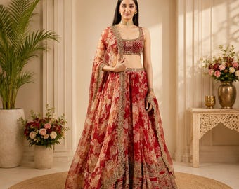 May include: A two-piece lehenga set featuring a sleeveless blouse and a floor-length skirt in a deep red floral print. The ensemble is accented with intricate gold embroidery along the borders and waistband, paired with a matching sheer dupatta.