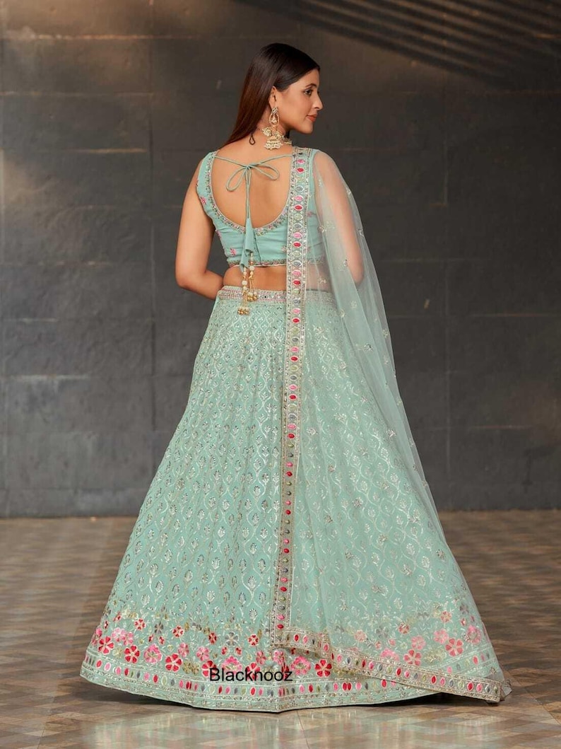 May include: A light green lehenga with intricate embroidery and a matching top. The outfit features a sheer dupatta and is adorned with pink and silver accents. The text "Blacknooz" is visible at the bottom.