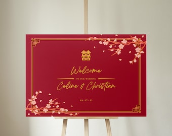 May include: Red wedding welcome sign with gold lettering and a traditional Chinese double happiness symbol. The sign reads "Welcome to our wedding, Celine & Christian, 09.17.23" and features a floral design with pink blossoms.