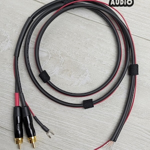 May include: A black audio cable with red accents, featuring two gold-plated RCA connectors and a spade lug terminal. The cable is coiled and secured with black hook-and-loop fasteners. The text END-TO-END AUDIO is visible in the top right corner.