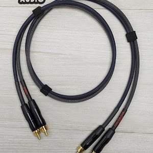 Puede incluir: Cables de audio trenzados en negro y azul, con conectores negros y puntas doradas. Los cables están asegurados con una correa de velcro negra. El texto "END-TO-END AUDIO" es visible.