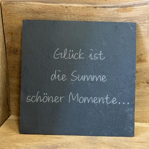 Könnte beinhalten: Schwarzes Schiefer-Schild mit weißer Aufschrift "Glück ist die Summe schöner Momente..."