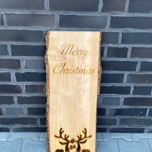 Könnte beinhalten: Ein Holzschild mit den Worten "Merry Christmas" und einem Rentier, das hinter dem Text hervorlugt.