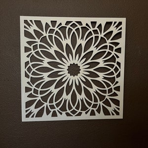Könnte beinhalten: Weiße Dekor-Schablone mit geometrischem Blumenmuster. Die Schablone ist quadratisch und weist ein sich wiederholendes Muster aus filigranen Linien und Kurven auf.